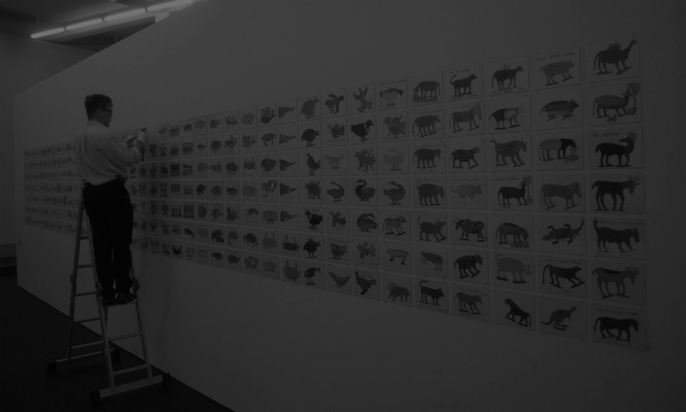 Ein Mann steht auf einer Leiter und betrachtet eine Wand mit Bildern von Tieren.
