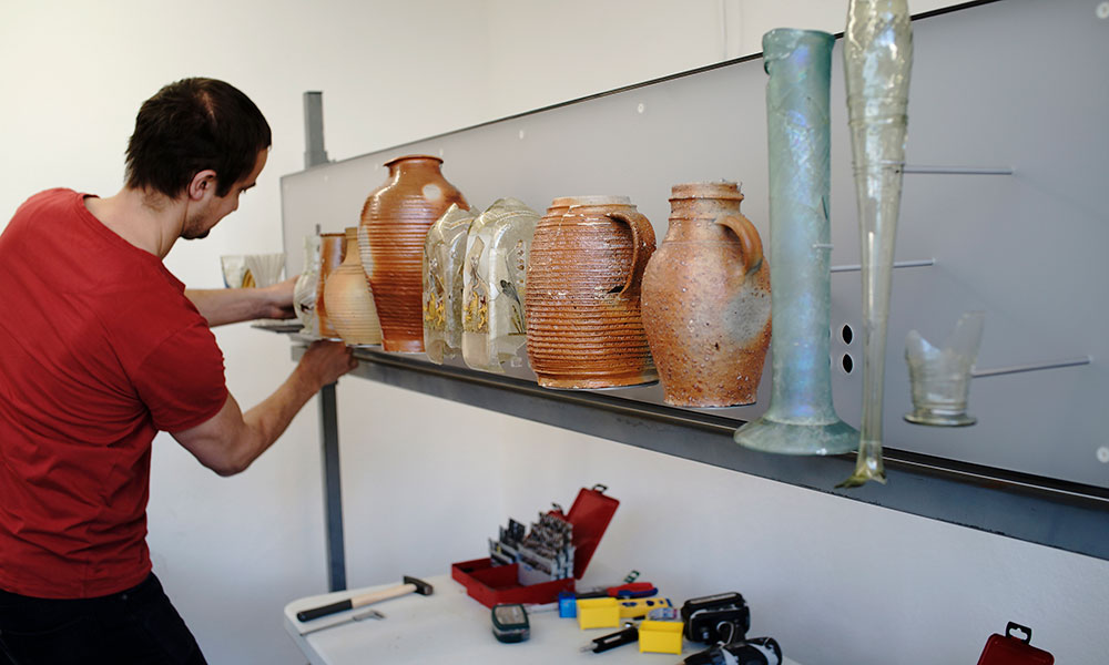 Ein Mann arbeitet an einem Regal, das mit vielen Vasen gefüllt ist.
